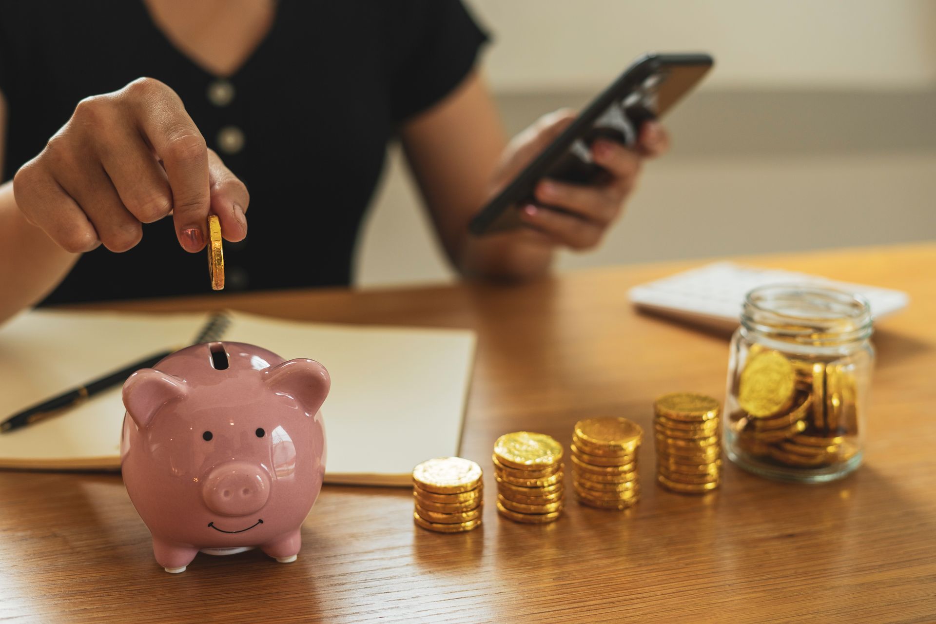 Frauen legen Münzgeld in Sparschweine und erstellen Einnahmen- und Ausgabenkonten auf ihren Smartphones Frauen legen Münzgeld in Sparschweine und erstellen Einnahmen- und Ausgabenkonten auf ihren Smartphones