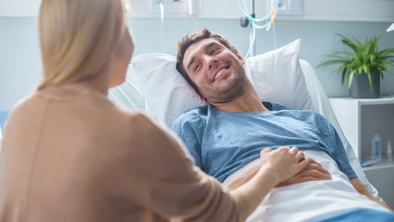 Mann liegt im Krankenhausbett und lächelt seine Frau an.
