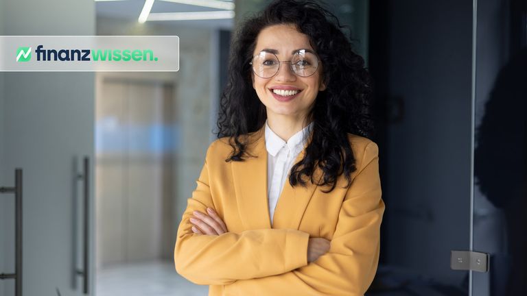Frau mit schwarzen Locken, Brille und gelbem Jackett steht frontal vor der Kamera