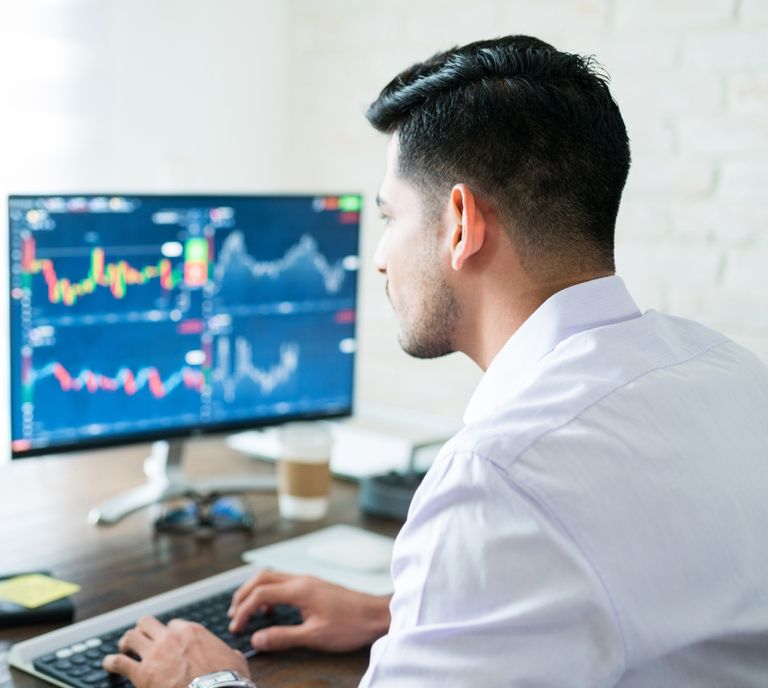 Trader arbeitet am PC, im Hintergrund Monitor mit Trading Charts