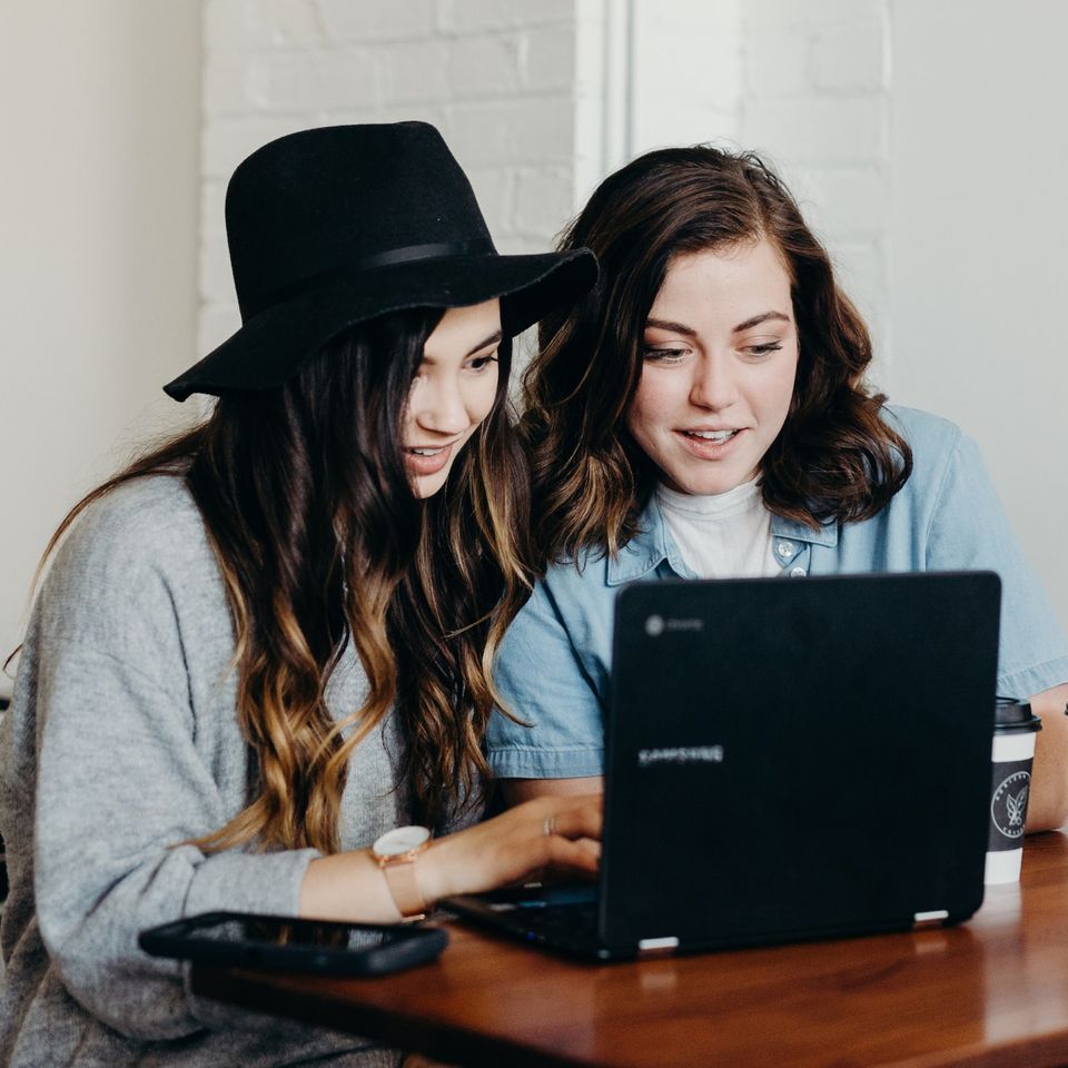 Zwei junge Frauen sitzen am Laptop und diskutieren über einen Artikel | © Unsplash/Brooke Cagle
